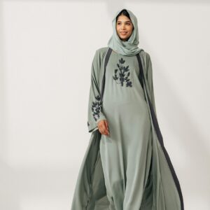 A fashionable adult woman models a sophisticated green abaya indoors, showcasing elegant design.