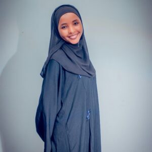 Portrait of a smiling woman wearing a hijab and abaya on a plain background.