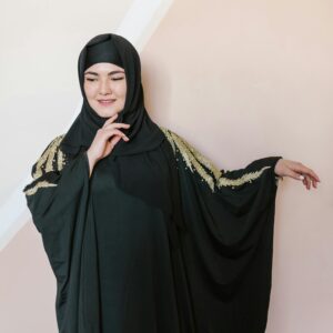 Graceful woman in a black abaya with gold embroidery poses elegantly indoors.